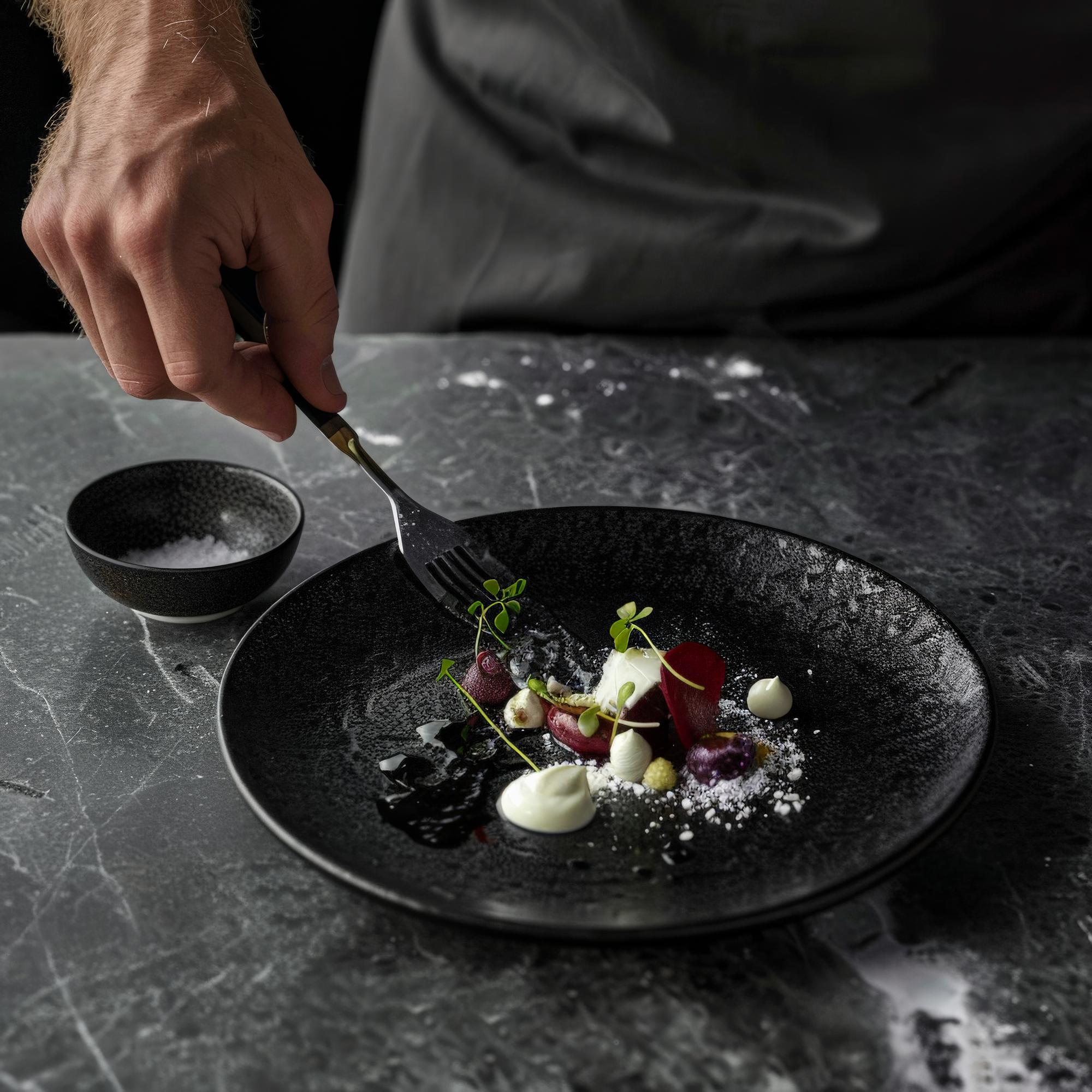 Chef arranging plated dish on dark table